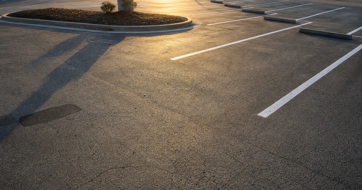 A freshly marked commercial lot at low sun, the new white stall lines running in converging rows from the curb to the wheel stops at the far end.
