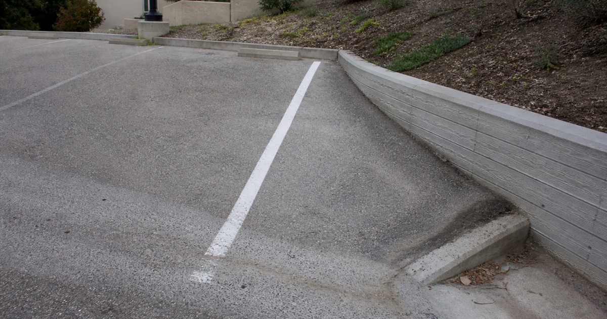 Fresh stall line running down the fall of a sloping Los Feliz commercial lot to a low retaining wall, a scoured drainage channel crossing it